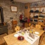 tavolo in apparecchiato per due con cibo e 2 bicchieri di vino rosso sullo sfondo uno scaffale pieno di bottiglie di vino