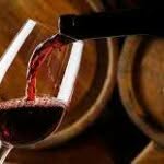 primo piano di bottiglia di vino rosso che viene versato in un calice sullo sfondo si intravedono due grosse botti