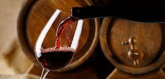 primo piano di bottiglia di vino rosso che viene versato in un calice sullo sfondo si intravedono due grosse botti
